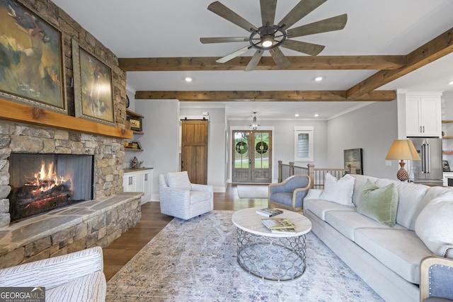 living room featuring a stone fireplace, dark wood-type flooring, beamed ceiling, and ceiling fan