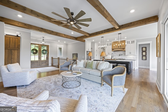 living room featuring beam ceiling, ceiling fan with notable chandelier, and light wood-type flooring