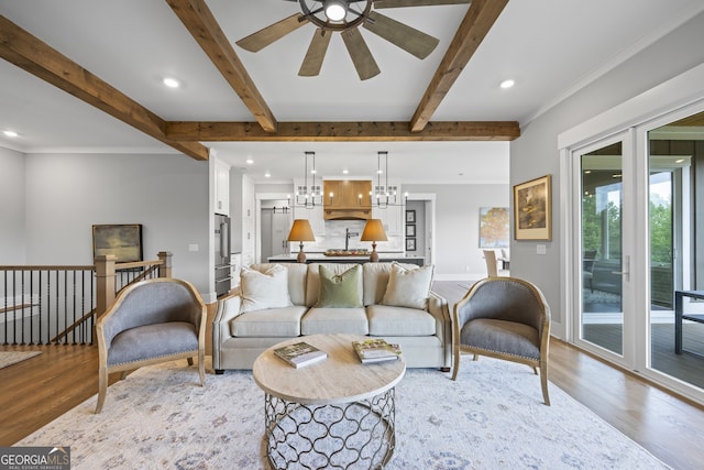 living room featuring beam ceiling, hardwood / wood-style flooring, ceiling fan with notable chandelier, and crown molding