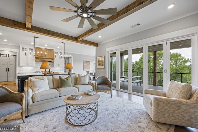 living room featuring beamed ceiling, french doors, ceiling fan with notable chandelier, and a barn door