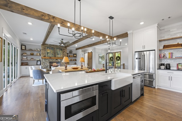 kitchen with light hardwood / wood-style flooring, stainless steel appliances, a stone fireplace, pendant lighting, and a kitchen island with sink