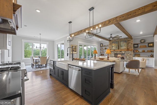 kitchen with dark hardwood / wood-style flooring, appliances with stainless steel finishes, a stone fireplace, decorative light fixtures, and a center island with sink