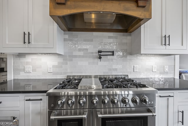 kitchen with dark stone counters, white cabinetry, premium range hood, range with two ovens, and tasteful backsplash