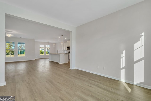 unfurnished living room with ceiling fan, sink, and light wood-type flooring