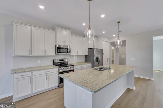 kitchen featuring light stone counters, appliances with stainless steel finishes, pendant lighting, a kitchen island with sink, and white cabinets