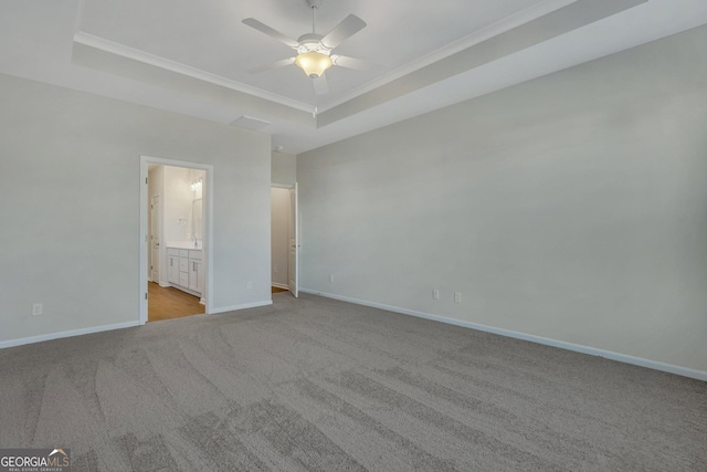 unfurnished bedroom featuring a raised ceiling, ornamental molding, connected bathroom, and light colored carpet