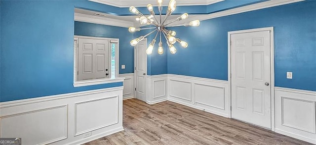 empty room with crown molding, an inviting chandelier, a raised ceiling, and hardwood / wood-style floors