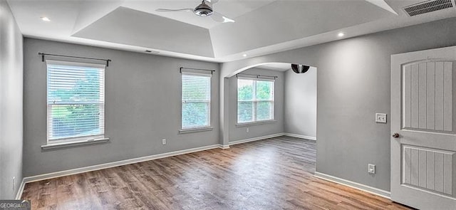 empty room with ceiling fan, a tray ceiling, and hardwood / wood-style flooring