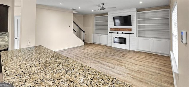 kitchen featuring a large fireplace, light hardwood / wood-style flooring, ceiling fan, ornamental molding, and built in shelves