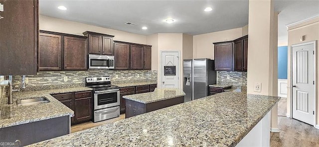 kitchen with sink, light stone counters, backsplash, and appliances with stainless steel finishes