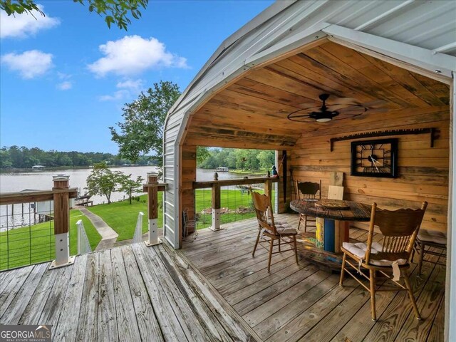 wooden terrace featuring a water view, ceiling fan, and a lawn