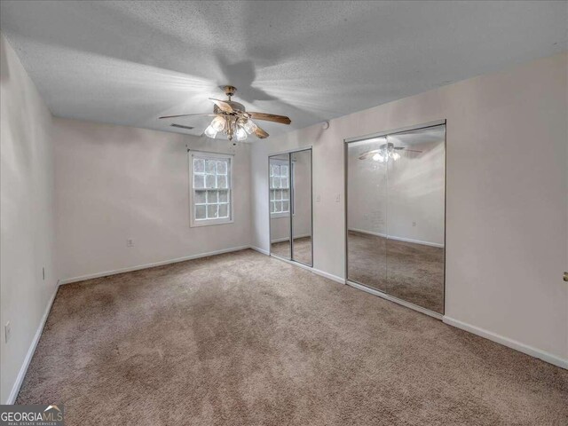 unfurnished bedroom with multiple closets, carpet, ceiling fan, and a textured ceiling