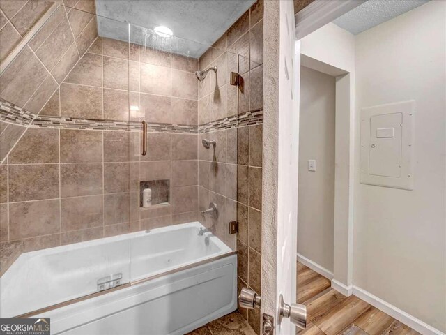 bathroom with a textured ceiling, hardwood / wood-style floors, and tiled shower / bath combo