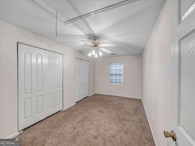 unfurnished bedroom with two closets, ceiling fan, a textured ceiling, and carpet floors