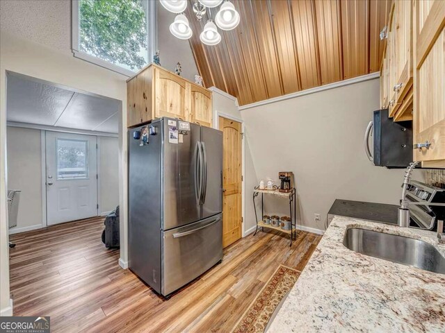 kitchen with light stone countertops, light hardwood / wood-style floors, an inviting chandelier, lofted ceiling, and appliances with stainless steel finishes