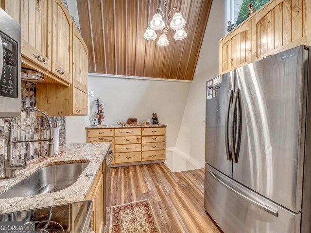 kitchen featuring light stone countertops, light wood-type flooring, backsplash, lofted ceiling, and stainless steel refrigerator