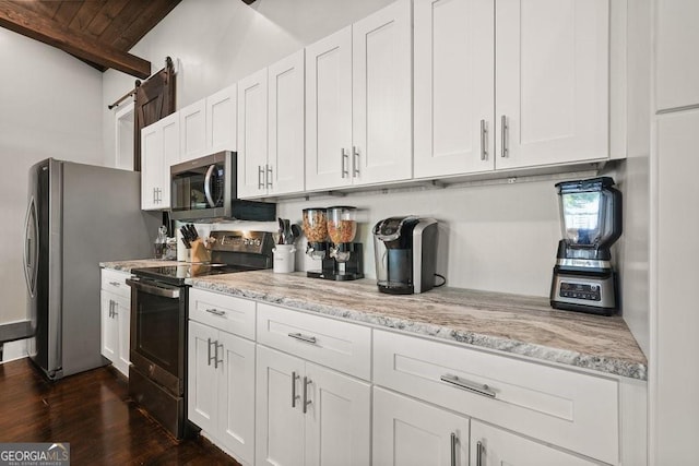 kitchen with dark wood-type flooring, white cabinetry, appliances with stainless steel finishes, light stone countertops, and beamed ceiling