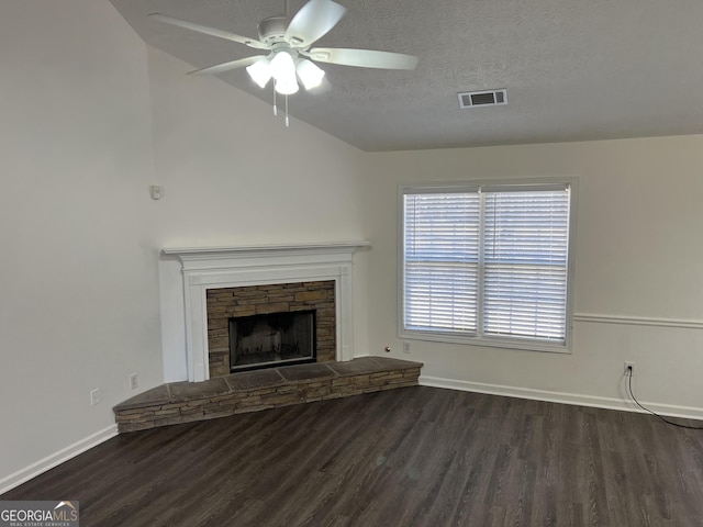 unfurnished living room with ceiling fan, dark wood-type flooring, a stone fireplace, vaulted ceiling, and a textured ceiling