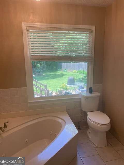 bathroom with a wealth of natural light, tile flooring, toilet, and a bathing tub