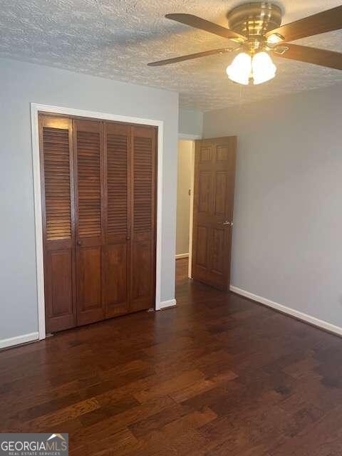 unfurnished bedroom featuring dark wood-type flooring, a closet, ceiling fan, and a textured ceiling