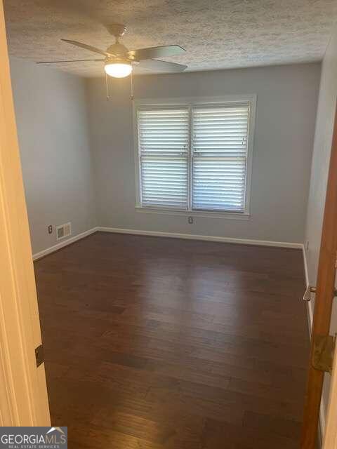 empty room with a textured ceiling, dark wood-type flooring, and ceiling fan