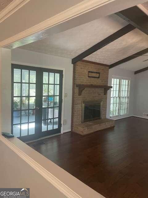 unfurnished living room featuring brick wall, a brick fireplace, a wealth of natural light, beam ceiling, and wood-type flooring