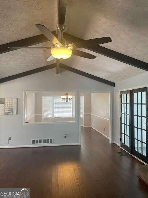 unfurnished living room featuring ceiling fan with notable chandelier, vaulted ceiling with beams, and dark wood-type flooring