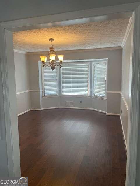 unfurnished room with crown molding, a chandelier, and dark wood-type flooring