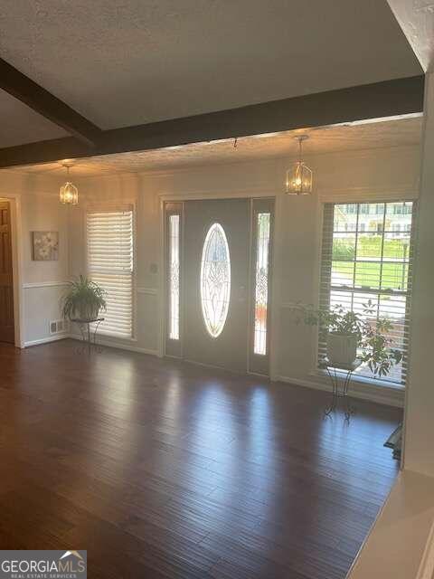 entrance foyer with beamed ceiling, an inviting chandelier, and dark hardwood / wood-style floors