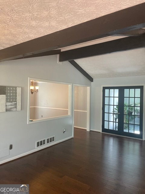 empty room featuring french doors, lofted ceiling with beams, dark wood-type flooring, and a textured ceiling