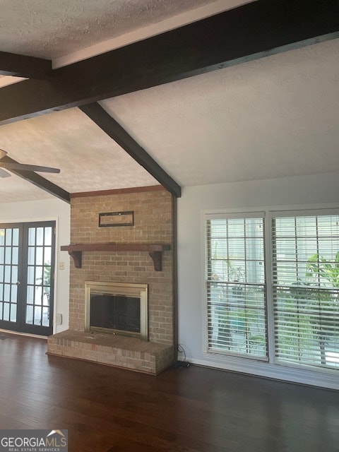 unfurnished living room with brick wall, a brick fireplace, dark hardwood / wood-style flooring, vaulted ceiling with beams, and a textured ceiling