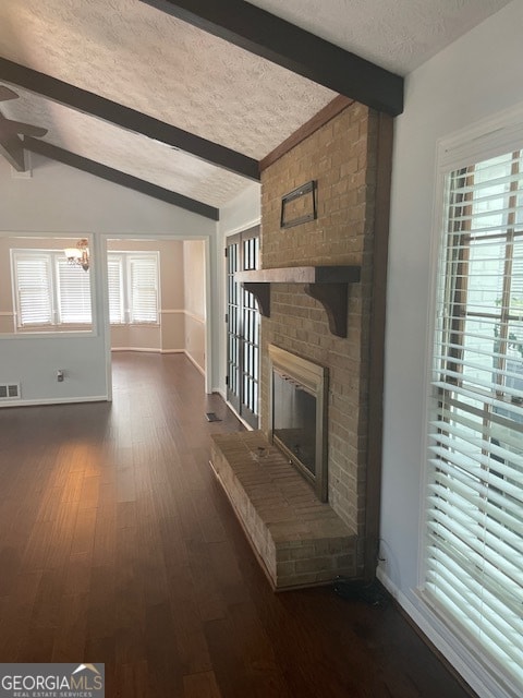 unfurnished living room featuring brick wall, a fireplace, vaulted ceiling with beams, dark wood-type flooring, and a textured ceiling