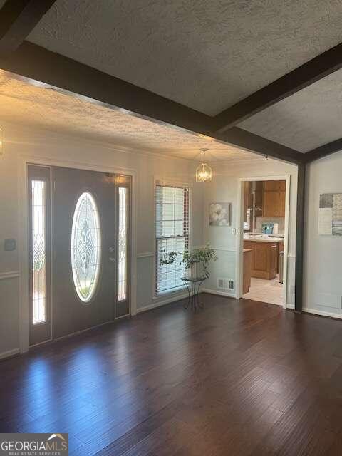 foyer featuring beam ceiling, a chandelier, a textured ceiling, and dark hardwood / wood-style flooring