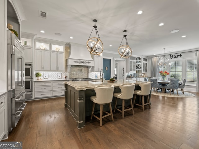 kitchen featuring backsplash, dark hardwood / wood-style flooring, custom range hood, and a kitchen island with sink