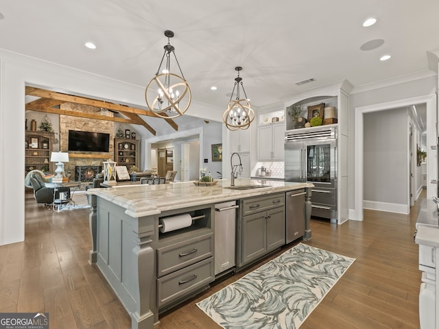 kitchen with a fireplace, a kitchen island with sink, dark hardwood / wood-style floors, light stone counters, and decorative light fixtures