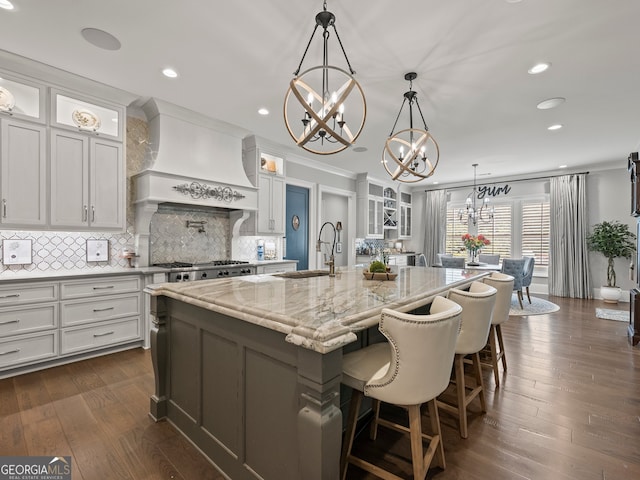 kitchen featuring a center island with sink, pendant lighting, dark wood-type flooring, premium range hood, and white cabinets