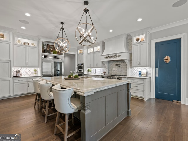 kitchen featuring tasteful backsplash, a large island with sink, custom range hood, dark hardwood / wood-style flooring, and appliances with stainless steel finishes