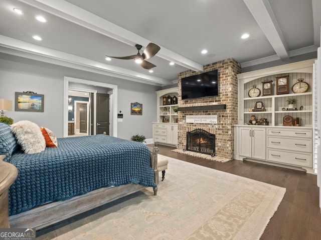 bedroom featuring beamed ceiling, ceiling fan, dark wood-type flooring, and a brick fireplace