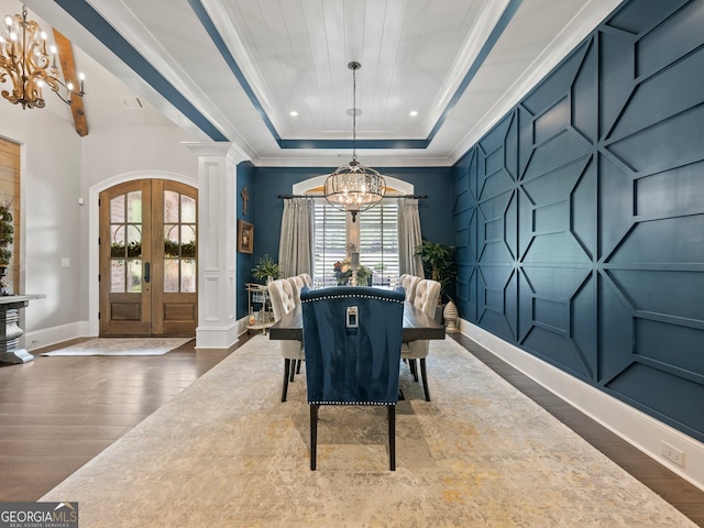 dining room with a tray ceiling, crown molding, decorative columns, dark wood-type flooring, and an inviting chandelier