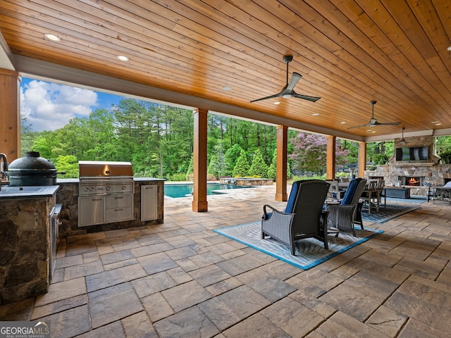 view of patio with ceiling fan, a grill, exterior kitchen, and an outdoor stone fireplace