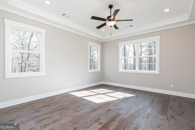 empty room with ceiling fan, a tray ceiling, crown molding, and dark wood-type flooring