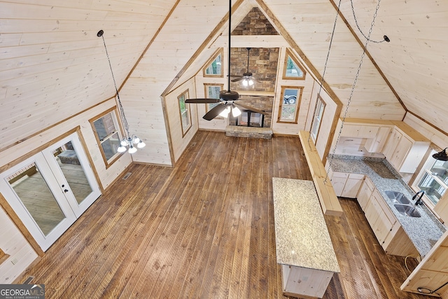 unfurnished living room featuring dark wood-type flooring, wood walls, sink, ceiling fan, and vaulted ceiling