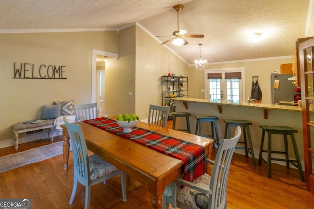 dining room featuring hardwood / wood-style floors, a textured ceiling, vaulted ceiling, ceiling fan with notable chandelier, and ornamental molding