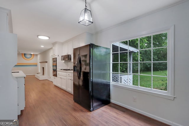 kitchen with hanging light fixtures, light hardwood / wood-style flooring, white cabinets, and black appliances