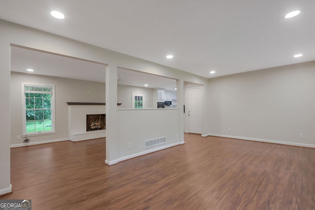 unfurnished living room with dark wood-type flooring and a brick fireplace