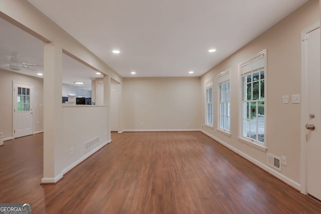 unfurnished living room with a wealth of natural light, dark wood-type flooring, and ceiling fan