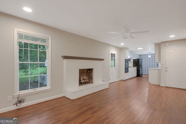 unfurnished living room with ceiling fan, hardwood / wood-style flooring, and a brick fireplace