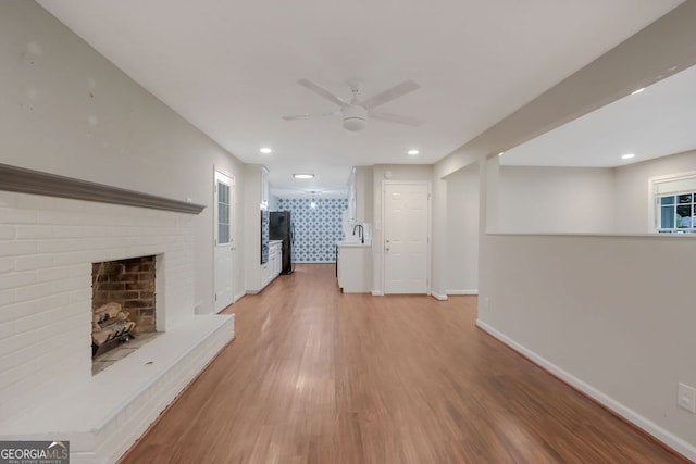 unfurnished living room with light wood-type flooring, sink, a brick fireplace, and ceiling fan