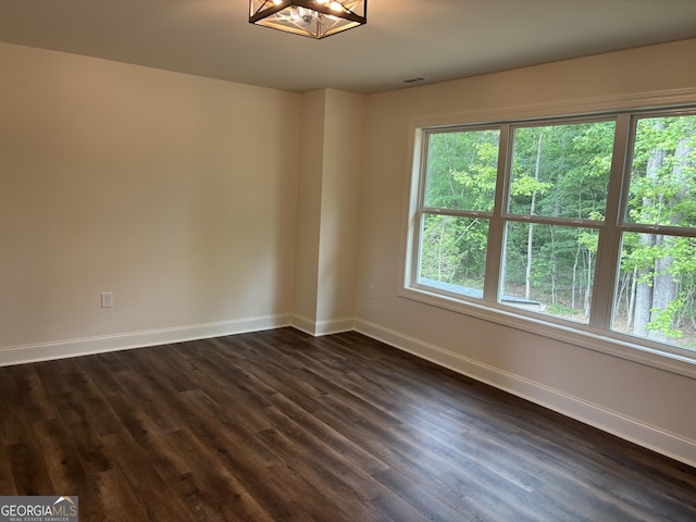 unfurnished room with baseboards, dark wood-type flooring, a chandelier, and visible vents