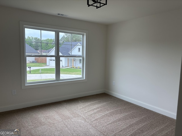 carpeted empty room featuring baseboards, a chandelier, and visible vents
